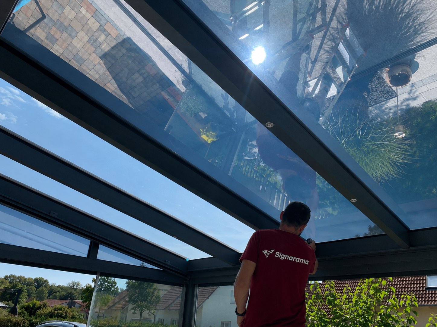 Signarama-Monteur bringt Sonnenschutzfolie an einem Terrassendach an